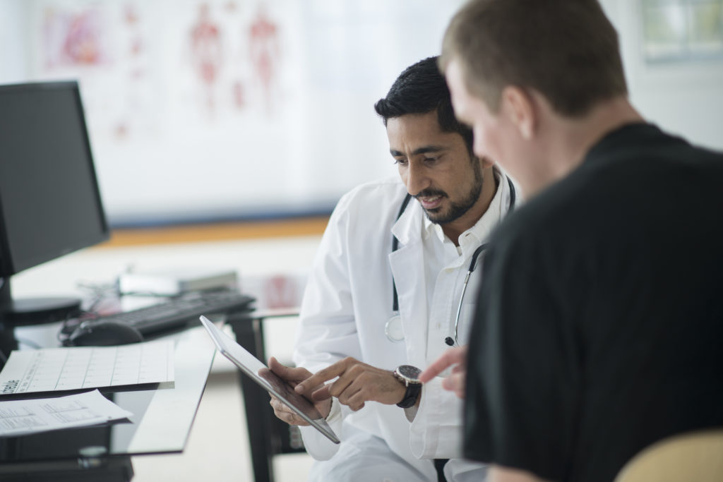 A doctor is going over the patients records and charts with him.