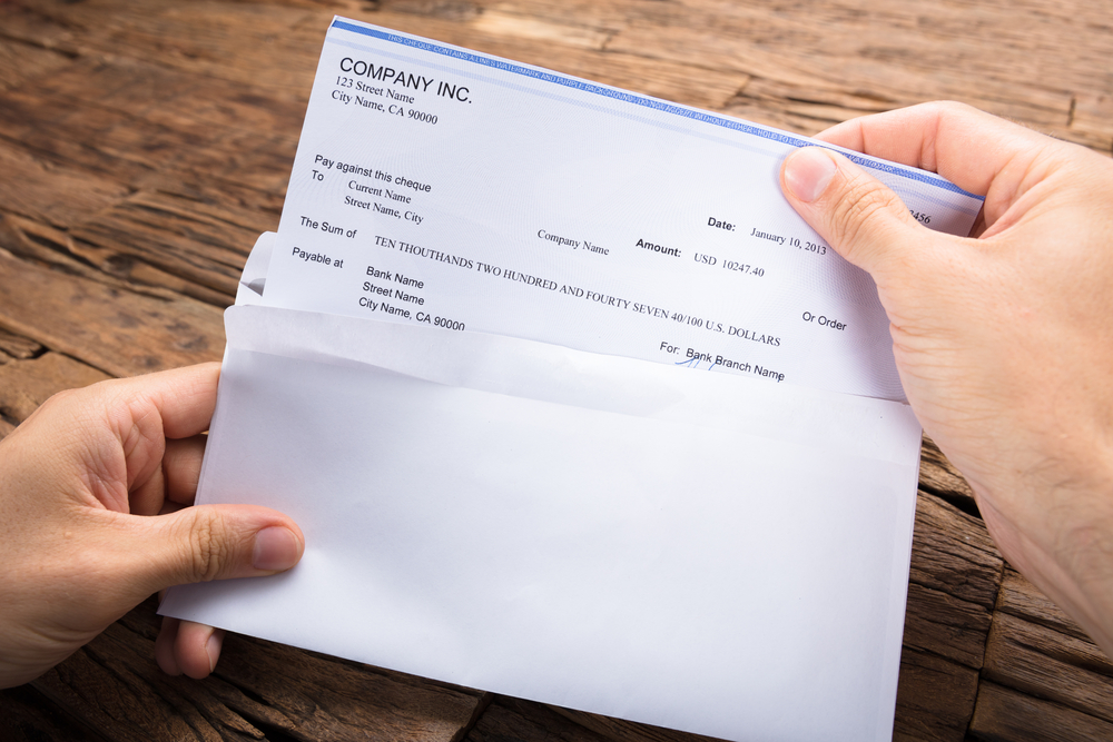 Cropped,Hands,Of,Businessman,Holding,Cheque,At,Wooden,Table